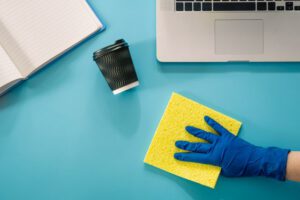 A hand in a rubber glove wipes the workplace, flat lay.